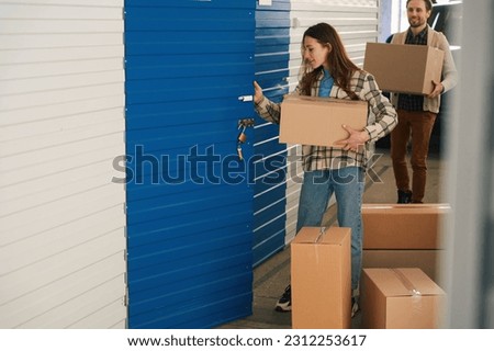 Woman and man with big cardboard boxes into warehouse with self storage unit