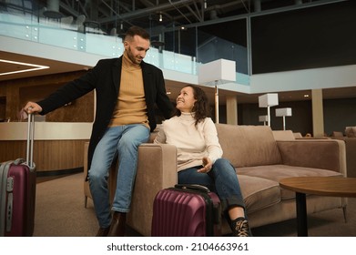 Woman and man in casual clothes with suitcases sitting on armchair in the international airport terminal lounge, looking at each other, discussing forthcoming flight, waiting for airplane departure
