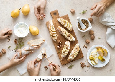 Woman, man and child are cooking sweet open sandwiches with ricotta cheese, fresh pears, walnuts and honey on kitchen table for family breakfast, overhead view - Powered by Shutterstock