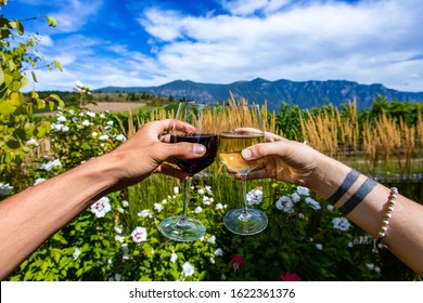 Woman And Man Couple Hands Holding And Toasting White And Red Wine Glasses, Drinking Tasting Wines Against Flowers Plants, Okanagan Valley Nature