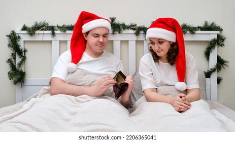 A Woman And A Man With An Empty Wallet Without Money On A Bed Decorated For Christmas And New Year, Family Couple In Home Bedroom