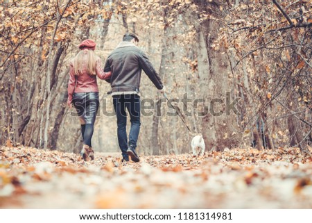 Woman and man in the fall strolling with their dog in the park embracing each other in love