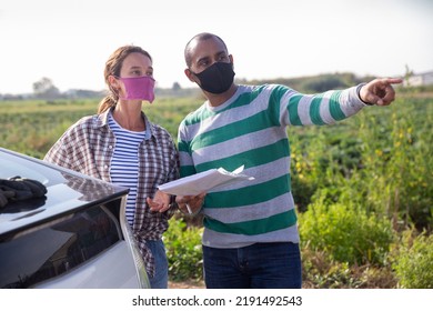 Woman And Man Farm Workers Wearing Face Masks For Spread Viral Disease Discussing Papers Standing Near Car Outdoors