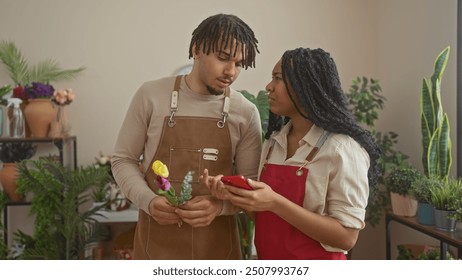 A woman and man florists in aprons working together, using a smartphone, inside a flower shop with plants. - Powered by Shutterstock