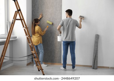 Woman and man hanging wallpaper in room - Powered by Shutterstock