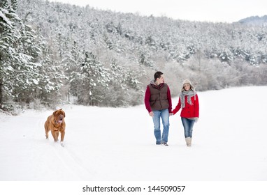 Woman And Man Are Having Walk With Dog In Winter Snowy Countryside