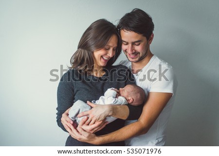 Woman and man holding a newborn. Mom, dad and baby. Close-up. Portrait of young smiling family with newborn on the hands. Happy family on a background. 