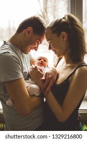 Woman And Man Holding On Hands A Newborn. On The Background Window. Mom, Dad And Baby. Portrait Of Young Family. Happy Family Life. Man Was Born. Vertically Framed Shot.