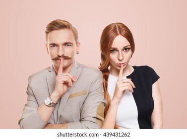 Woman And Man Keep Secret. Couple Shows Hush Sign, Adultery, Relationship Issue, Marriage Cheating Concept. Secret Love, Jealousy. Mystery, Privacy, Intimacy. Young Beautiful Couple Isolated At Pink