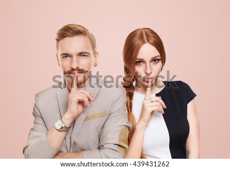 Woman and man keep secret. Couple shows hush sign, adultery, relationship issue, marriage cheating concept. Secret love, jealousy. Mystery, privacy, intimacy. Young beautiful couple isolated at pink
