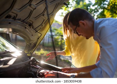 The Woman And The Man Are Repairing The Car. The Couple Looks Under The Hood Of The Car. Auto Mechanic And Female Customer. A Man Mechanic And Woman Customer Look At The Car Hood And Discuss Repairs.