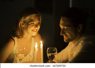 A woman and man share a joke over a glass of white wine at a candle lit table.