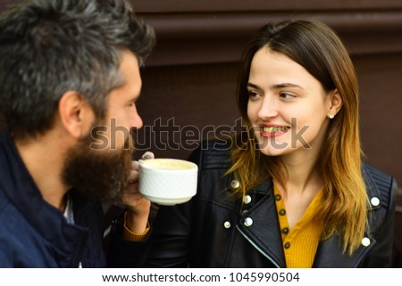 Woman and man with smiling faces have date at cafe. Girl and bearded guy have coffee on brown terrace background. Couple in love drinks espresso on coffee break. Hot beverage and lunch time concept