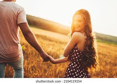 A woman and a man in walking across the field holding hands on a sunny day. Redhead woman smiling at camera. Summer vacation. Wheat field.