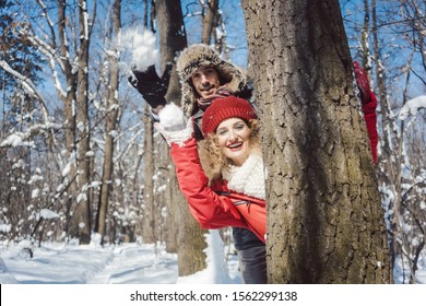 Woman And Man In Winter Throwing Snowball At The Camera Hiding Behind A Tree