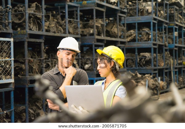 Woman and man work together,\
diversity of Asian engineer worker woman hold laptop, look at\
Caucasian  engineer man while he doubt data on laptop in\
factory-warehouse