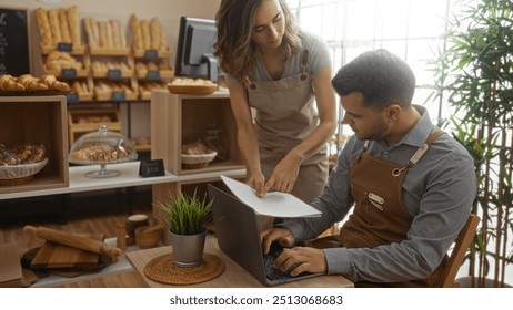 Woman and man working together in a bakery shop, with fresh baked goods displayed on shelves and tables, reviewing documents on a laptop. - Powered by Shutterstock