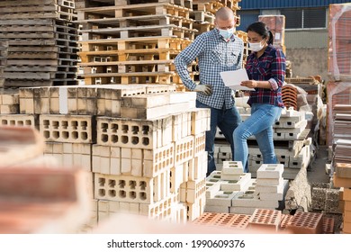 Woman Manager In Face Mask Discussing Order List With Man Worker At Warehouse Of Building Materials