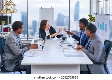 Woman manager is showing annual report chart to her African American colleagues in the executive meeting for next year plan with city skyline background for global business and investment - Shutterstock ID 2082705955