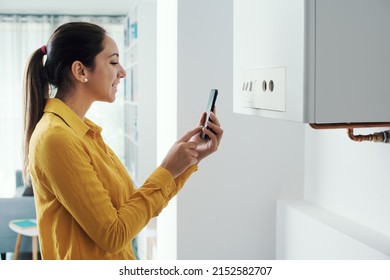Woman managing and programming her smart boiler using her smartphone, smart home concept