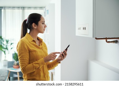 Woman managing and programming her smart boiler using her smartphone, smart home concept