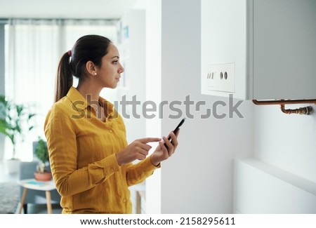 Woman managing and programming her smart boiler using her smartphone, smart home concept
