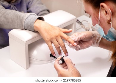 Woman Manicurist Master In Gloves Is Applying Top Coat On Pink Gel On Client's Nails In Beauty Salon, Hands Closeup. Manicure Nail Paint. Nail Polish. Hygiene Care About Nails. Beauty Procedure