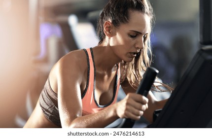 Woman, marathon training and fitness in gym on elliptical machine for health, wellness and cardio endurance. Cyclist, exercise bike and performance on equipment, power challenge and intense workout - Powered by Shutterstock