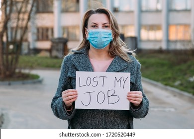 Woman in mask holds sign lost my job. Concept of job loss due to COVID-19 virus pandemic. Female stands against background of business center