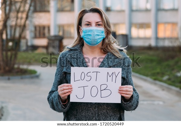 Woman in mask holds sign lost my job. Concept of\
job loss due to COVID-19 virus pandemic. Female stands against\
background of business\
center