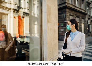 Woman with mask looking at a closed fashion clothes storefront.Clothing shopping during coronavirus outbreak shutdown.COVID-19 quarantine apparel retail store closures.Small business loss concept.