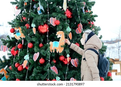 A Woman In A Mask Looks At The Decor On The Christmas Tree In The Park.