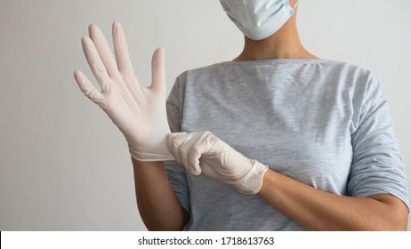 Woman With A Mask Putting On White Sterile Latex Surgical Gloves.