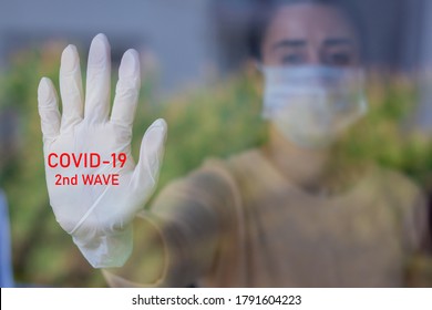 Woman In Mask Stretches Out Her Gloved Hand. The Glove Writes Covid-19 2nd Wave.