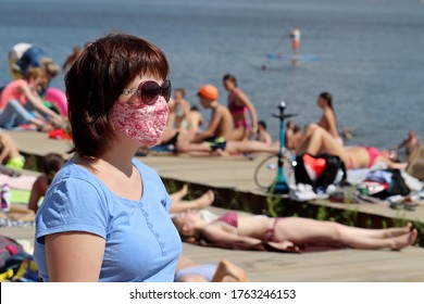 Woman In A Mask And Sunglasses Standing On A Sunny Beach On Sunbathing People Background. Safety During Covid-19 Coronavirus Pandemic, Summer Leisure