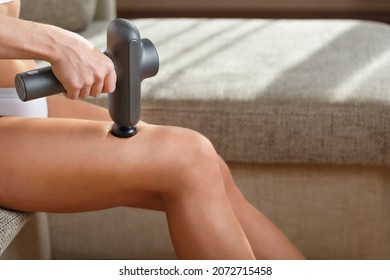 A Woman Massages Her Legs With An Automatic Pistol At Home. Shock Self-massage To Restore Fascia Muscles And Trigger Points