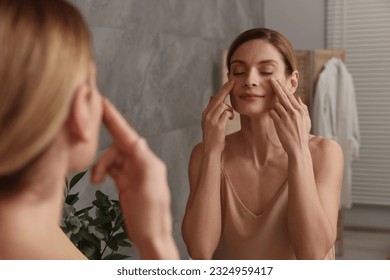 Woman massaging her face near mirror in bathroom - Powered by Shutterstock