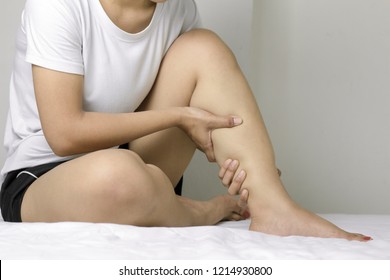 Woman massaging her leg because of pain. Pain the leg calf in concept of health. Sitting squeeze leg calf on the white bed.
