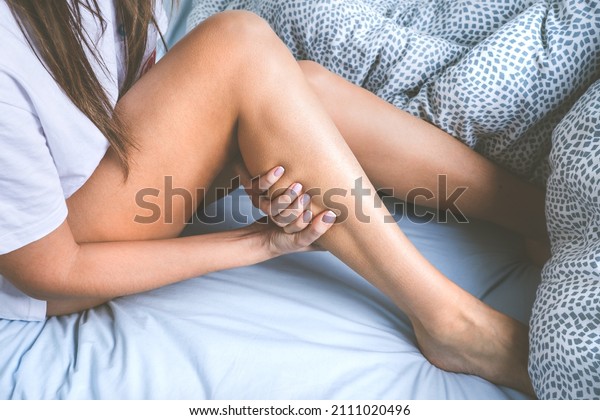 Woman massaging her leg\
because of leg muscle cramps. Muscle pain or leg pain while\
sleeping in the bed