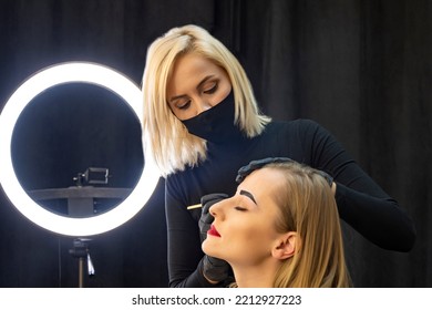 Woman A Master Makeup Artist In A Medical Mask Applies Makeup To A Woman's Face. Concept: Makeup For Women During The Coronavirus And Epidemic.