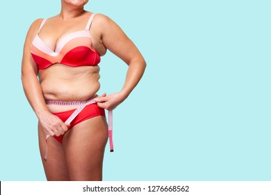 Woman Measures her Waist with a Measuring Tape. Blue Background. Isolated. Asian Girl Overweight. Female Model large Size Faceless in a Red bathing suit.        
