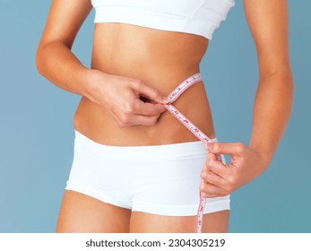Woman, measuring tape and lose weight, health and diet with waist size isolated on blue background. Healthy, tummy tuck and body measurement with female person in studio with wellness and fitness