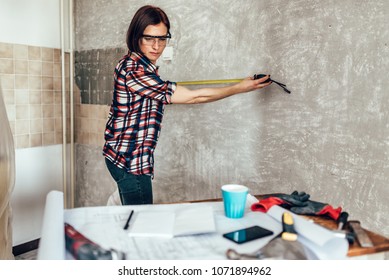 Woman measuring wall in kitchen and checking blueprints - Powered by Shutterstock