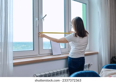 Woman measuring window with tape measure, tailoring service