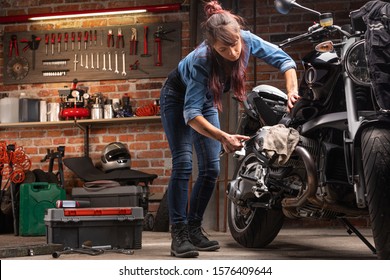 Woman Mechanic Or Biker Working On The Engine Of A Vintage Motorbike In A Large Neat Workshop