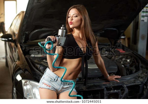 A woman mechanic blows off the\
dust from the screwdriver while sitting on the car\
hood