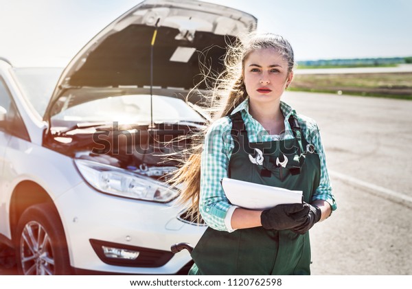 Woman\
mechanic with clipboard standing near broken\
car