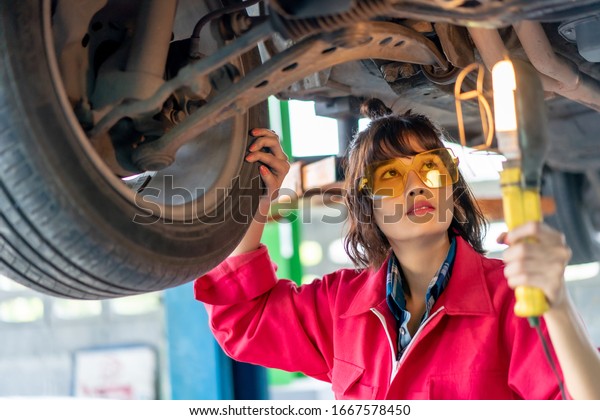 Woman Mechanic Examining Under the Car at
the Repair Garage. Asian young female checking and maintenance the
car. Asian young female car repair worker.
