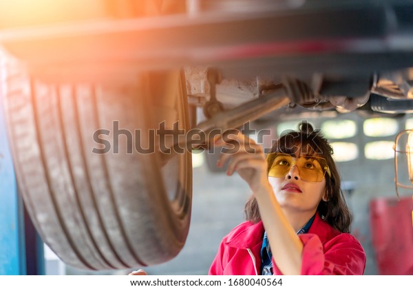Woman Mechanic Examining Under the Car at\
the Repair Garage. Asian young female checking and maintenance the\
car. Asian young female car repair worker.\
