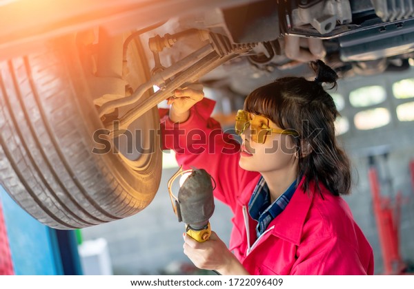 Woman Mechanic Examining Under the Car at\
the Repair Garage. Asian young female checking and maintenance the\
car. Asian young female car repair worker.\
